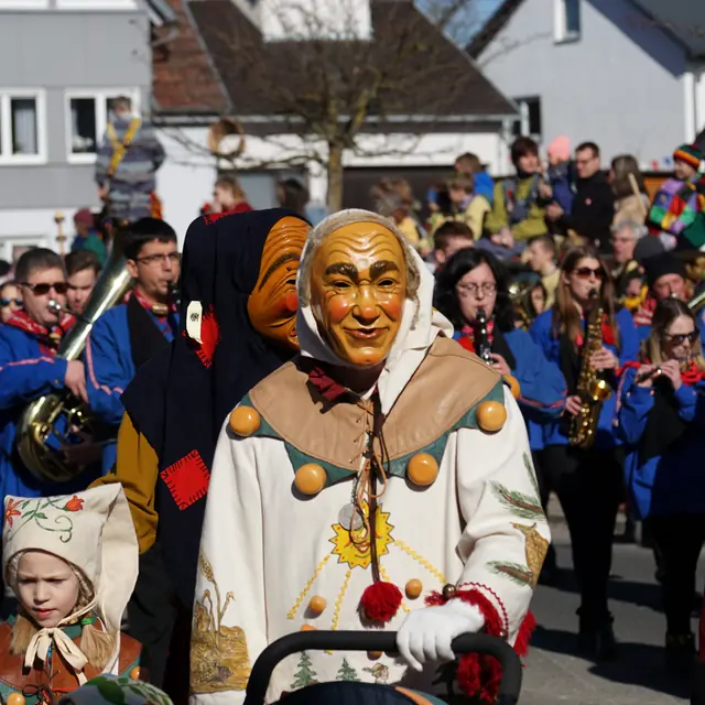 Weckazwinger und Schrättele beim Umzug, dahinter eine Musikkapelle in blauen Jacken