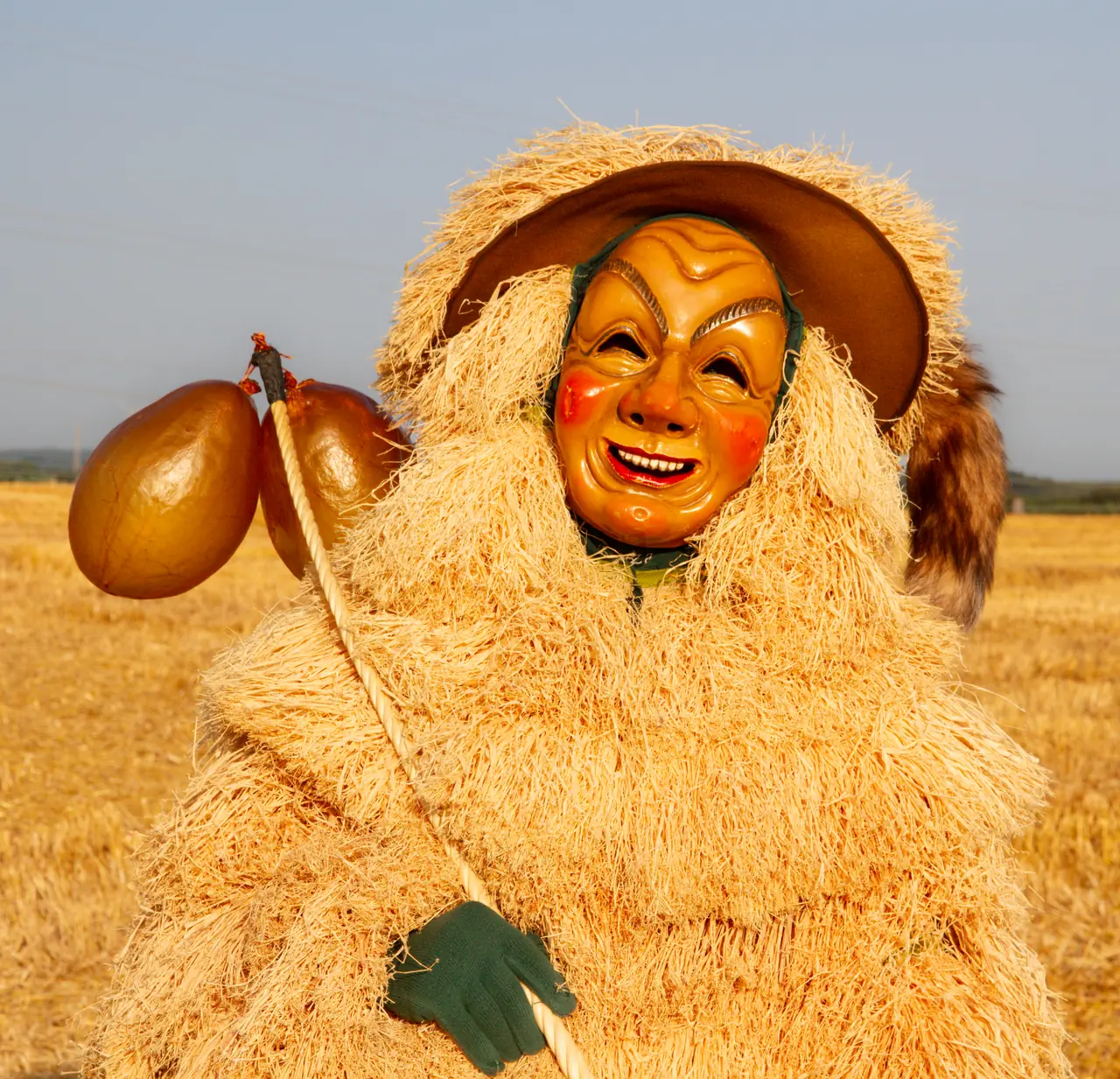 Strohbutz mit lachender Holzmaske und Hut im Kornfeld