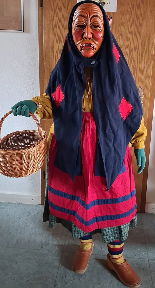 Schrättele mit grünen Handschuhen, Korb, hinten gebundener Schürze und Holzschuhen