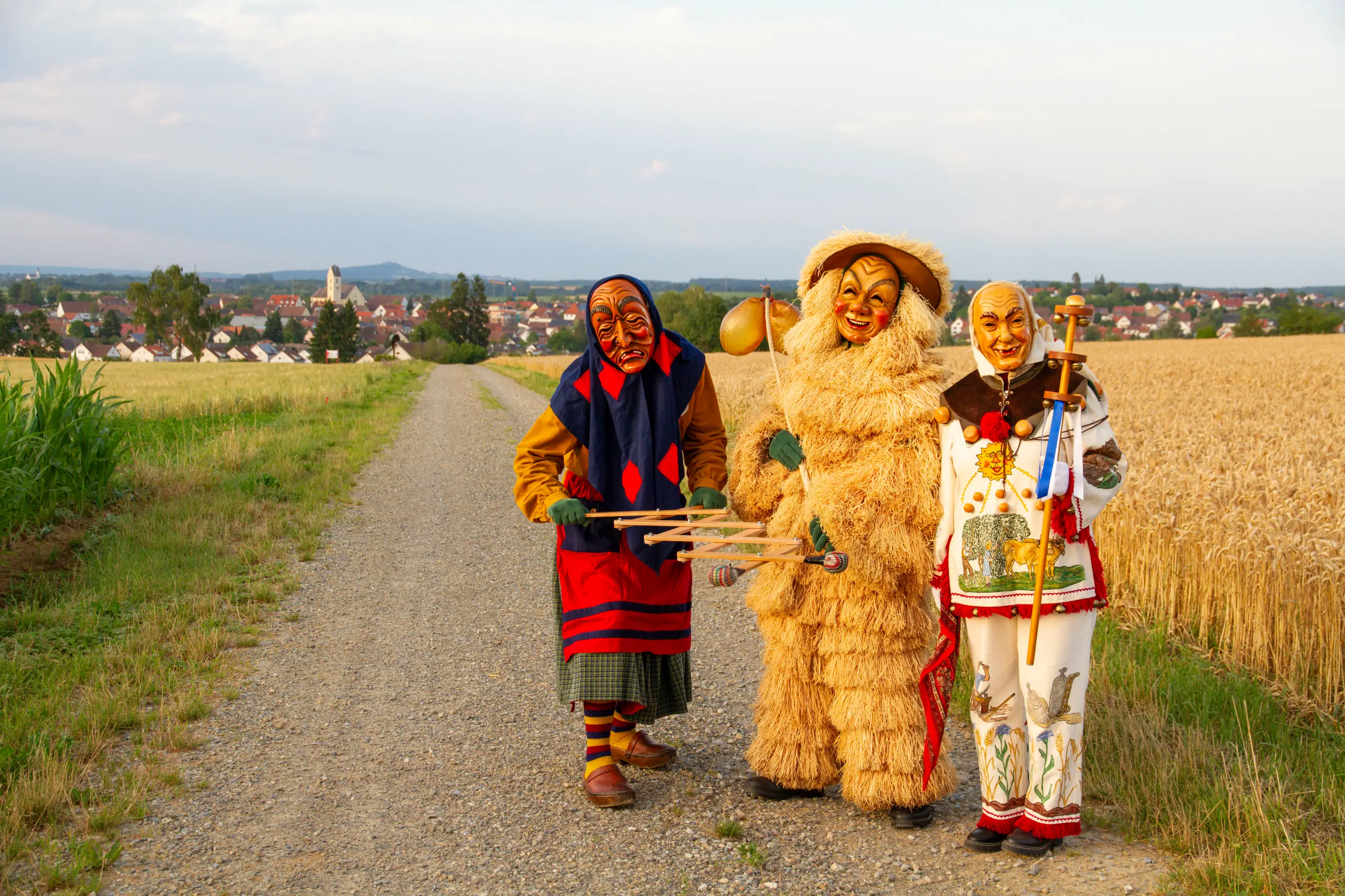 Schrättele, Strohbutz und Weckazwinger stehen nebeneinander auf einem Feldweg und schauen in die Kamera, dahinter Herbertingen